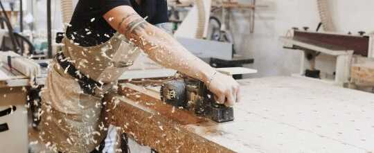 Carpenter working with electric planer on wooden plank in workshop. Craftsman makes own successful small business