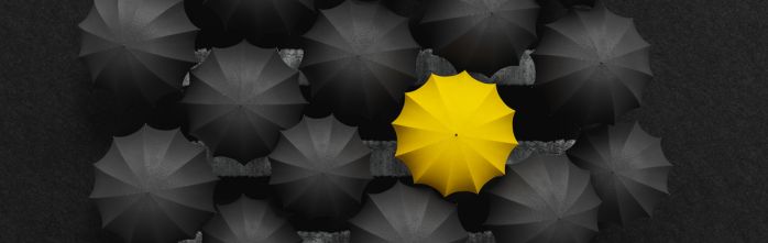 single yellow umbrella among black umbrellas